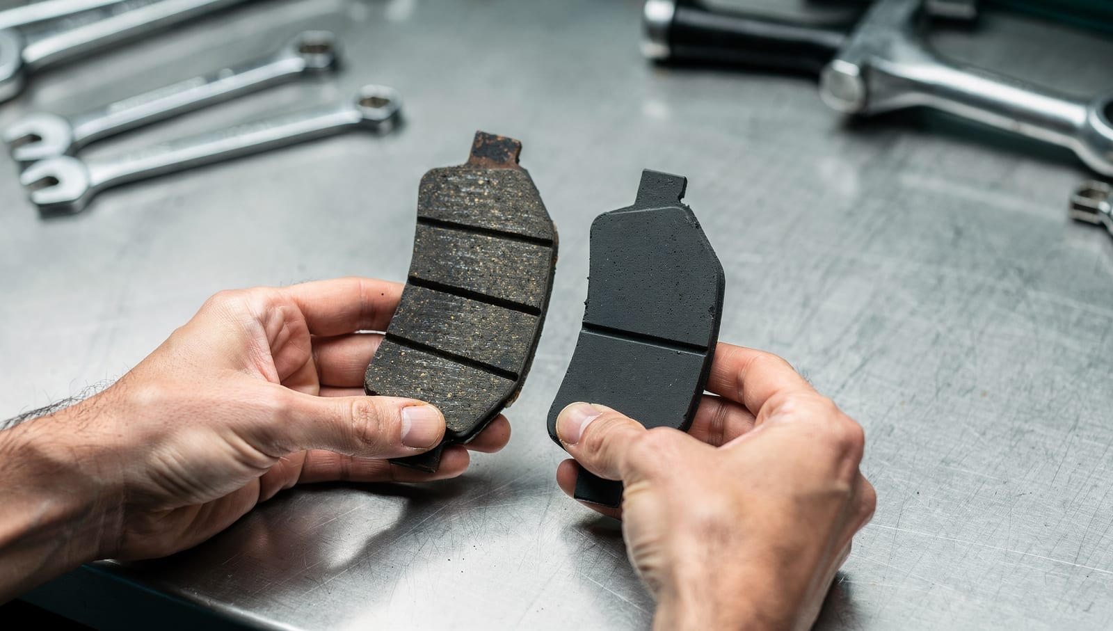 A mechanic holding a worn brake pad beside a fresh one